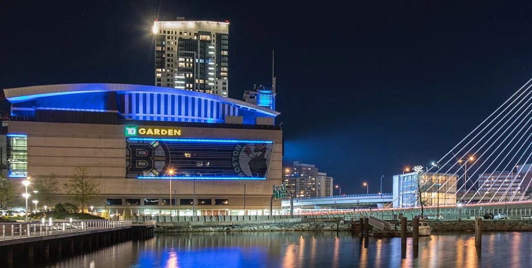 TD Garden lit up in blue at night beside the Zakim Bridge